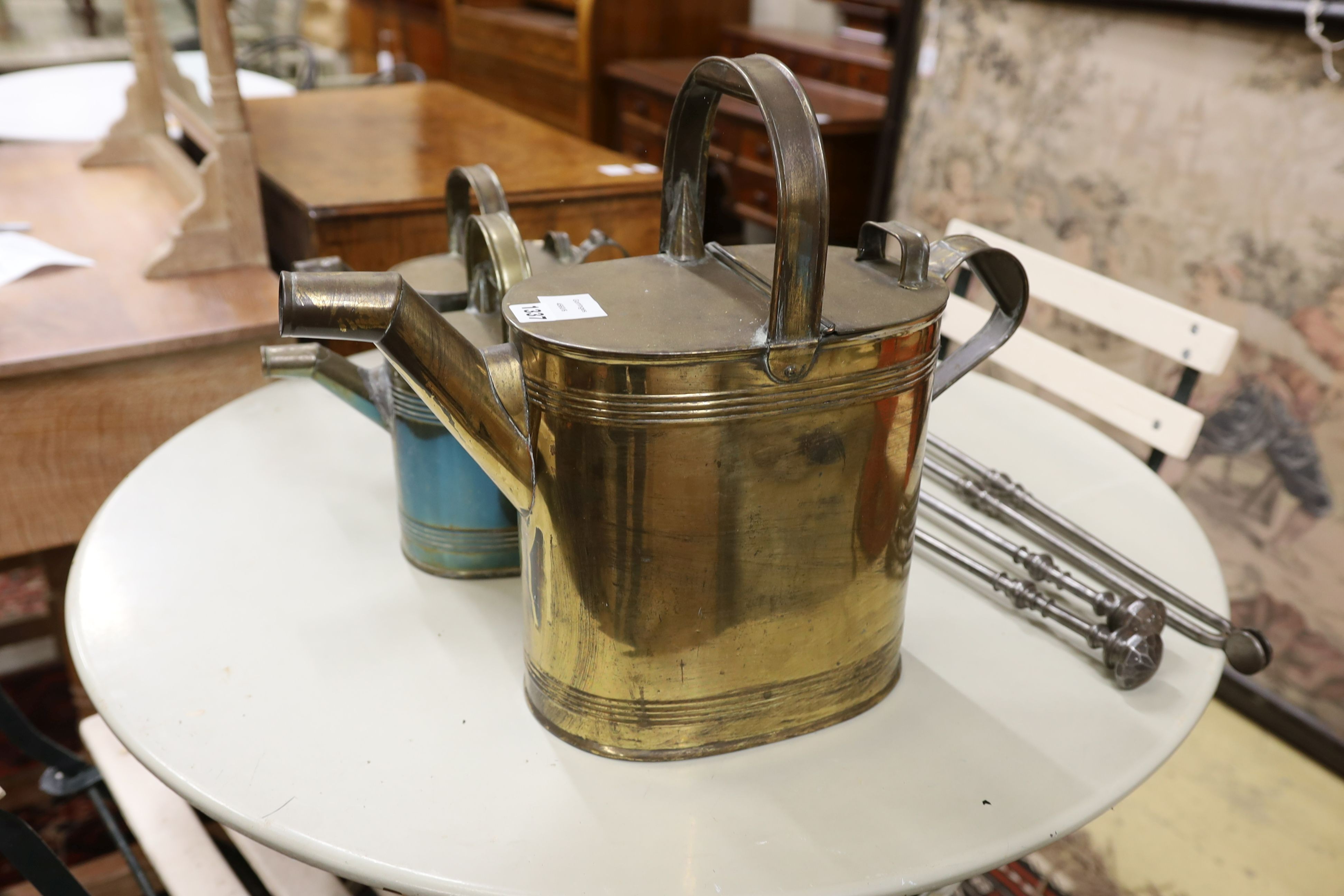 Three graduating brassed metal watering cans, largest height 40cm, together with a set of cast iron fire implements